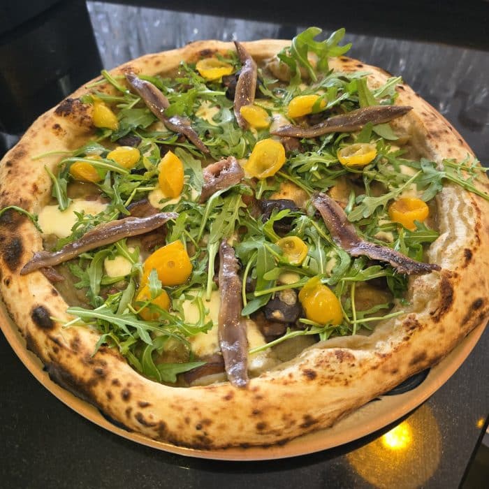 une pizza aux anchois napolitaine avec de la roquette et des tomates cerises jaunes