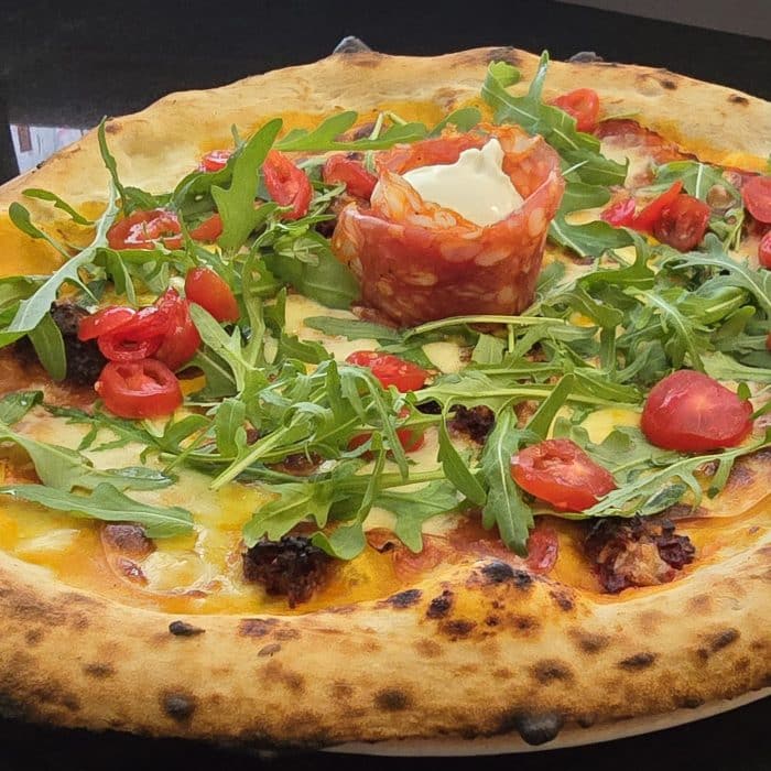 Une belle pizza napolitaine avec de la roquette, tomates cerise, charcuterie italienne et une boule de burrata au centre