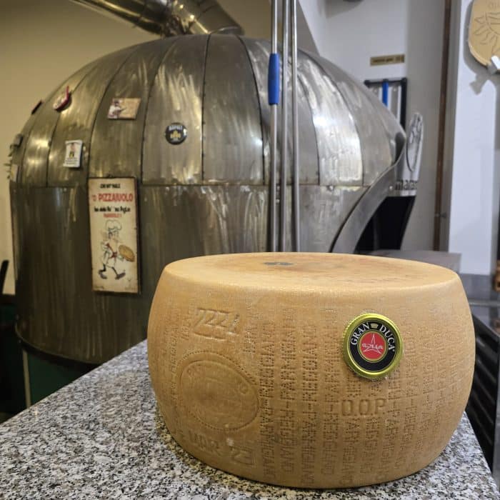 une tome de parmigiano regiano posée sur le plan de travail de la pizzeria avec le four en fond